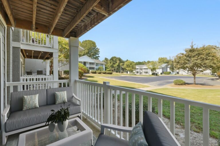 Charming apartment balcony with cozy seating overlooking a lush, green landscape and vibrant community setting.