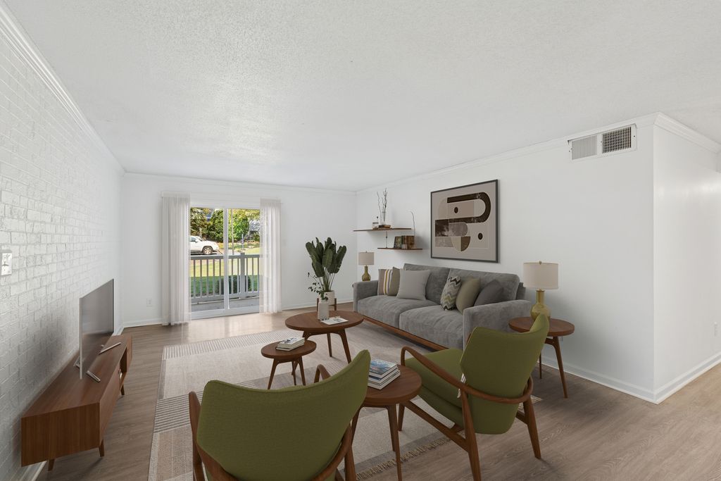 Elegant living room with modern furniture, featuring a cozy gray couch, stylish green chairs, and a large window overlooking lush greenery.